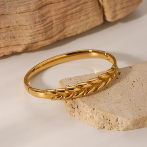 Elegant gold wheat pattern stainless steel bangle displayed on a natural stone surface