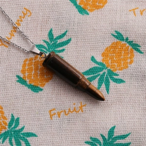 Tiger eye stone bullet pendant necklace with silver chain on patterned fabric background