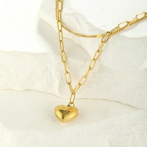Detailed view of layered gold heart necklace featuring a paperclip chain and small heart pendant