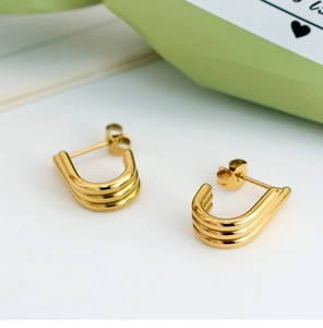 Macro shot of U-shaped gold earrings with triple-layered ribbed metal texture and pearls