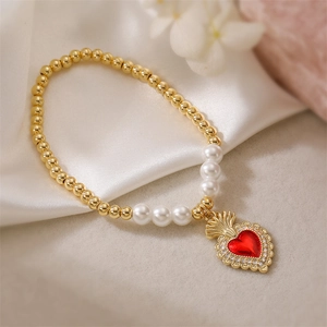 Detail of red sacred heart charm with zircons on gold and pearl beaded bracelet