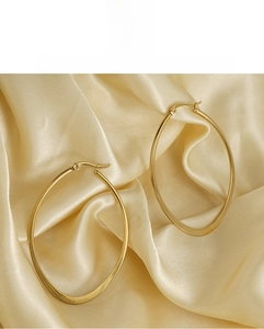 Macro shot of large oval gold plated titanium steel hoop earrings on champagne silk