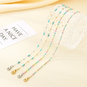 Detail of colorful beads and delicate chain anklets with lobster clasp on beige fabric
