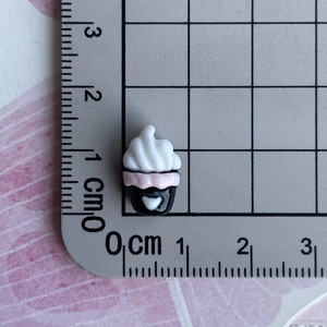 Macro shot of mini resin cupcake charm with pink and black details on a scale ruler