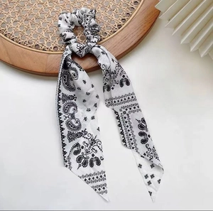 Detail showing a black and white paisley scrunchie with long ribbons on a wicker tray