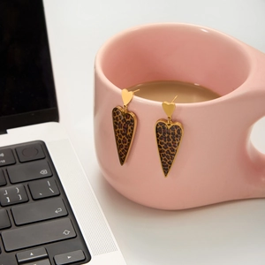 Detailed close-up of golden heart earrings with leopard print hanging on a pink ceramic mug