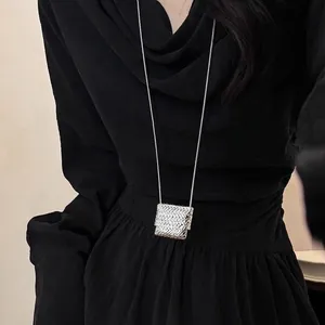 Close-up of a silver woven square pendant necklace worn by a model on black background