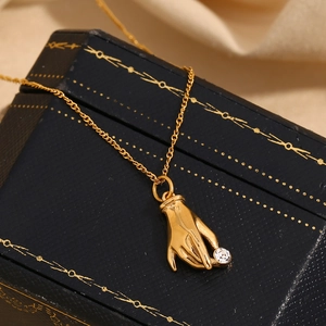 Macro shot of 18K gold plated hand-shaped pendant holding a round clear cubic zirconia
