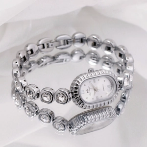 Detail of elegant silver oval quartz watch with crystal-encrusted bracelet on white silk