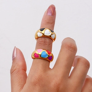 Close-up of wide gold-plated rings featuring colorful black, white and pink enamel hearts