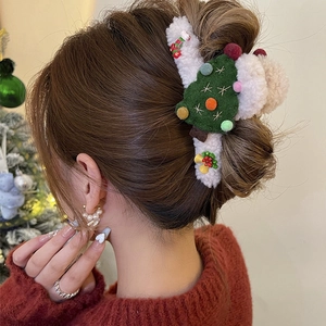 Plush Christmas reindeer hair claw clip with tree and bell detail on a female model