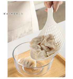 Macro detail of white ergonomic large kitchen skimmer lifting dumplings from a glass bowl