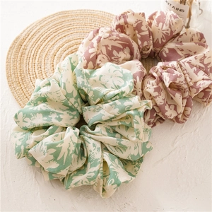 Oversized floral fabric scrunchies in pink and green patterns on a textured tabletop