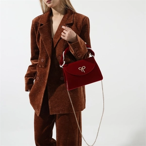 Detail of red velvet handbag with pearl handle, gold bow, and metal chain strap