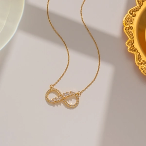 Golden infinity heart necklace with crystal stones on a minimalist beige background
