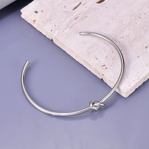 Detail of silver knot cuff bracelet displayed on minimalist stone texture and purple surface