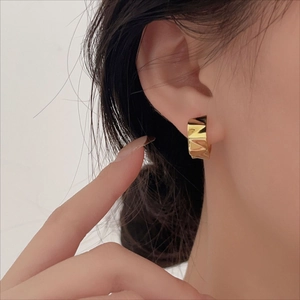 Close-up of geometric faceted 18K gold C-shaped earrings on a model ear