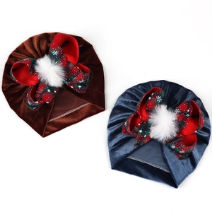 Detailed view of baby velvet hats with festive plaid bows and white faux fur pom-poms