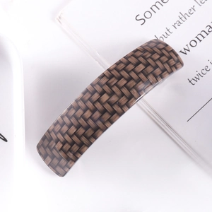 Detailed view of acetate hair clip with brown and grey woven pattern on white surface
