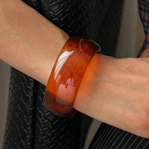Detail view of amber resin bangle against black woven leather texture background