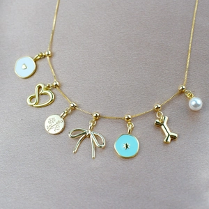 Gold multi-charm necklace with heart, star, bow, and pearl on champagne satin background