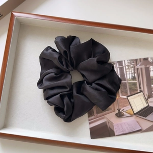 Detail of elegant black satin scrunchie with smooth silk texture and rich pleats on a tray