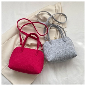 Detail of stone textured felt shell bags in fuchsia and grey on a cream blazer