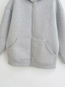 Detail of light gray hoodie showing metal zipper and symmetrical front patch pockets