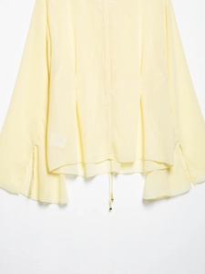 Detail of light yellow chiffon blouse featuring drawstring hem and gold metal charms