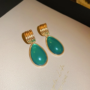 Detail of vintage gold C-shaped earrings with luxurious green teardrop gemstones