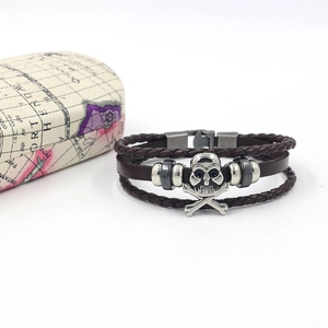 Close-up of vintage brown layered leather bracelet featuring silver skull and crossbones charm