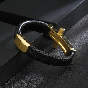 Detail of black braided leather bracelet with gold metal clasp on a textured surface