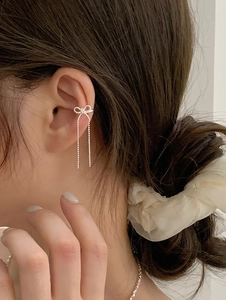 Detailed close-up of a silver bow ear cuff with long delicate chain tassels on a model
