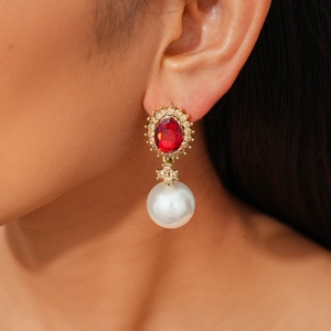 Detailed close-up of a vintage oval red gemstone and pearl drop earring on model