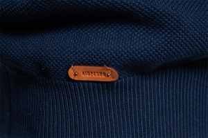 Detail der dunkelblauen Stricktextur mit braunem Lederetikett am Saum oder Ärmel