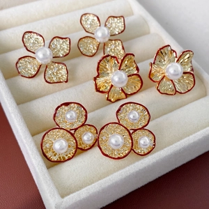 Nahaufnahme roter Blumenohrringe mit weißen Perlen und Goldakzenten auf Samttablett