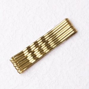 Macro shot of wavy gold metal hair pins stacked on a clean white textured surface