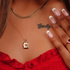 Close-up of golden square locket necklace with red heart gemstone and flat snake chain