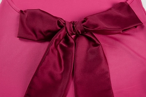 Detail of a large burgundy satin bow on the back of a pink dress with silk texture