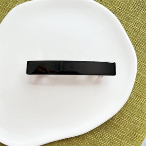 Close-up of a glossy black rectangular acetate hair clip with a sturdy metal spring