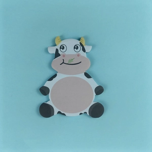 Close-up of cute cow-shaped sticky note with black spots and green grass detail