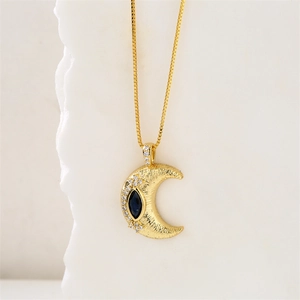 Détail d'un collier croissant de lune doré avec gemme bleue et petits zircons