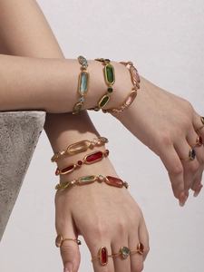 Close-up of vintage gold bracelets with emerald and ruby glass stones on model wrist
