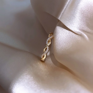 Close-up of twisted gold ring with zircon stones on luxurious champagne silk fabric