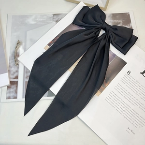 Detail of elegant black matte satin oversized bow hair clip with long ribbons on a magazine