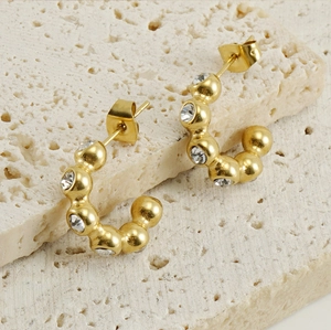 Detail of 18K gold-plated U-shaped earrings with clear zircons on beige stone