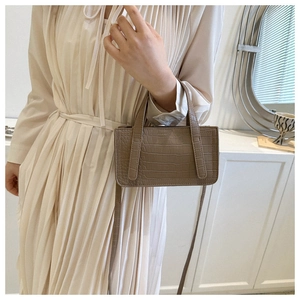 Detailed view of khaki crocodile-embossed small square bag with top handles on a model