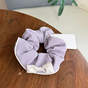 Detail of lavender floral scrunchie with white bow and contrast piping on wood