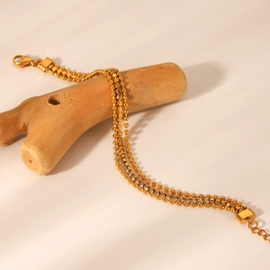 Three-layer gold stainless steel beaded chain bracelet displayed on natural wood