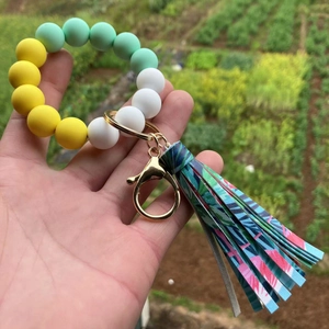 Silicone bead keychain bracelet with tropical palm leaf tassel held against green nature